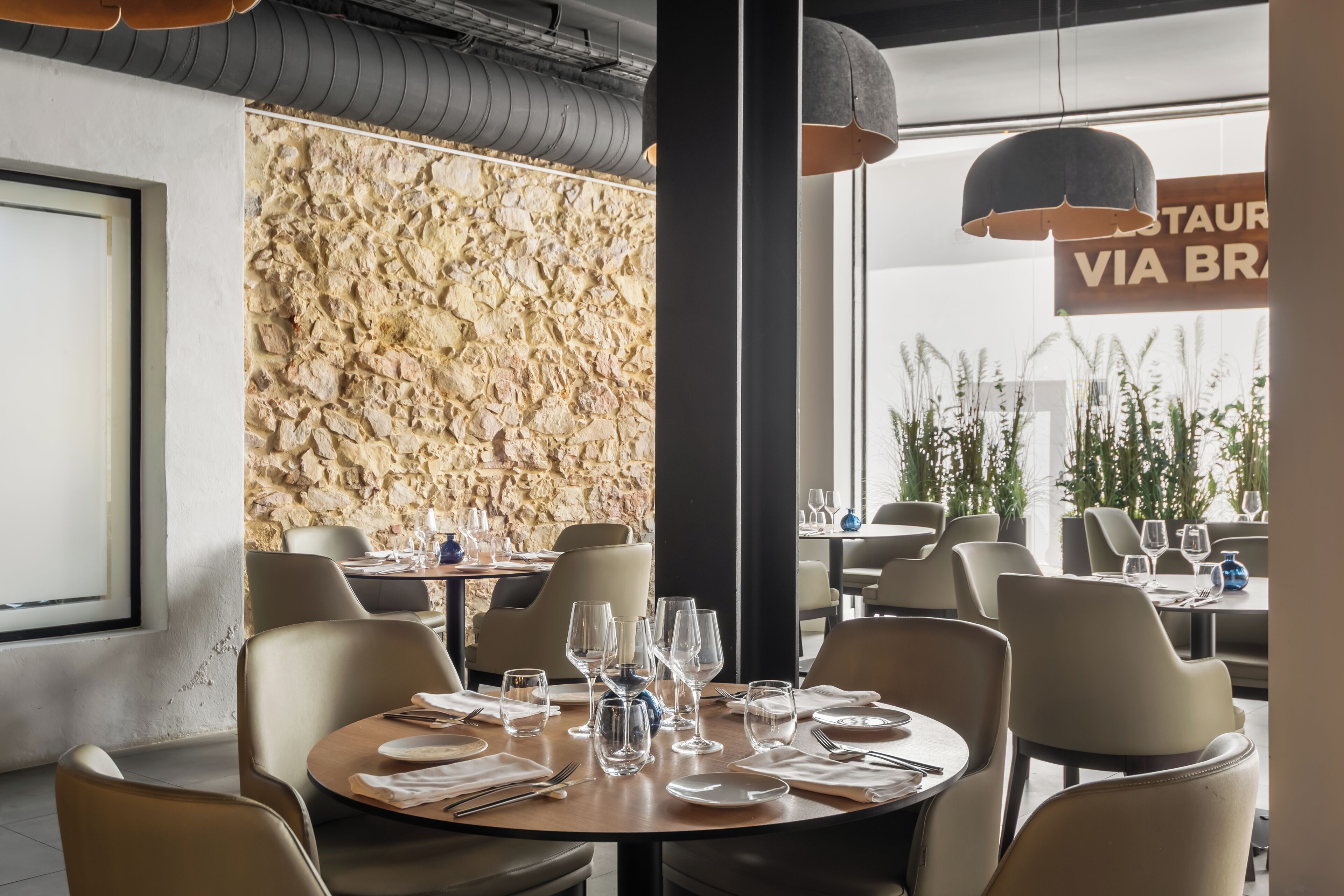 A restaurant interior with round tables, chairs, and a stone wall.