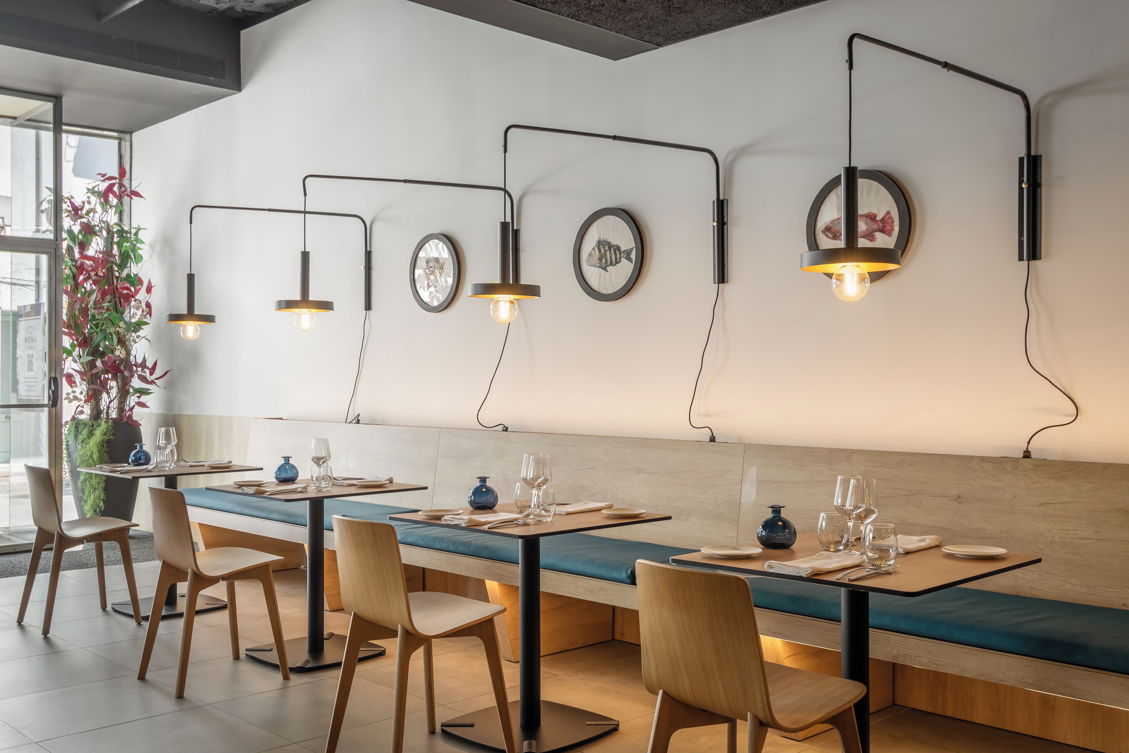 A restaurant with wooden tables and chairs, a long counter, and wall-mounted lights.