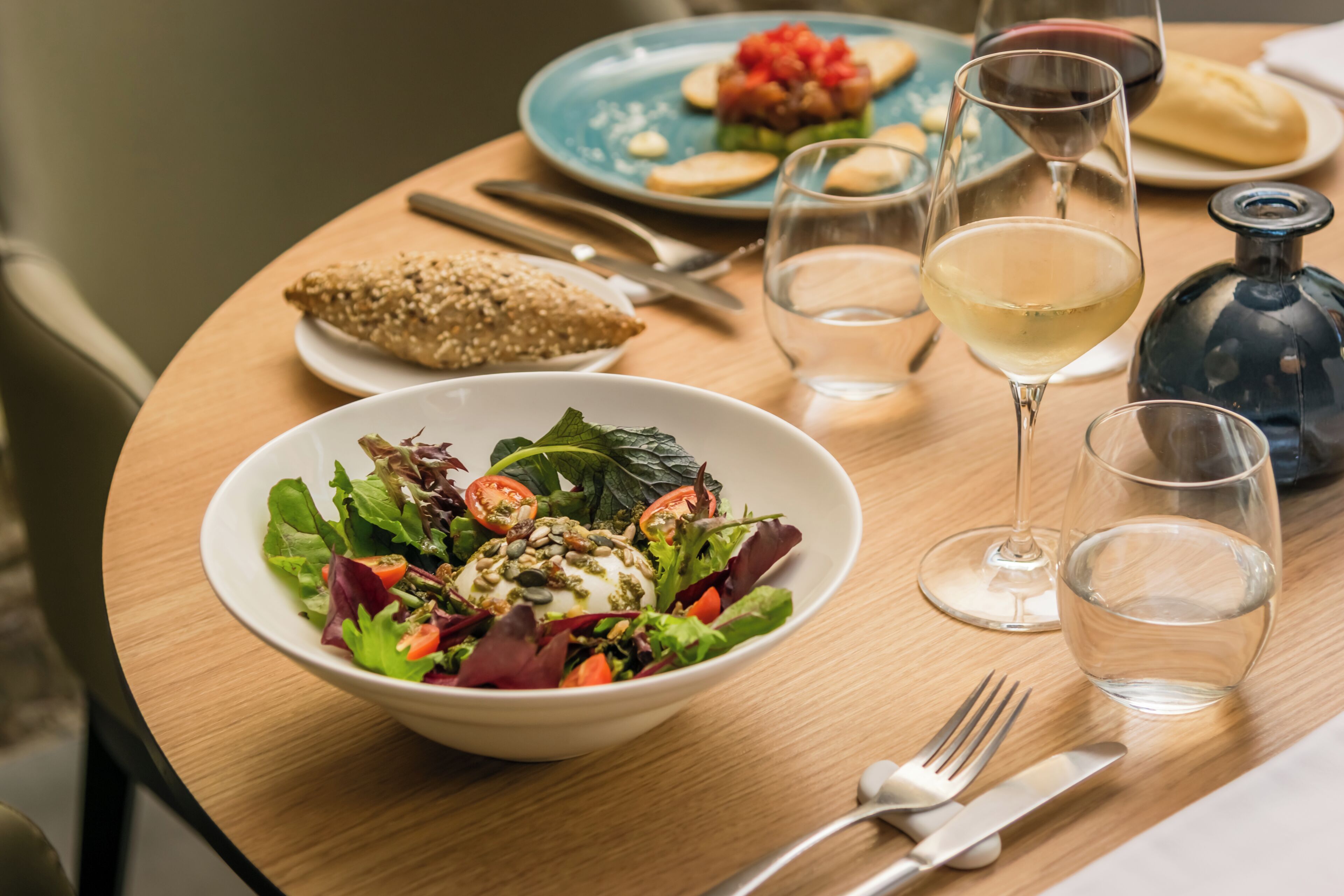 A dining table with a salad, bread, wine glasses, and cutlery.