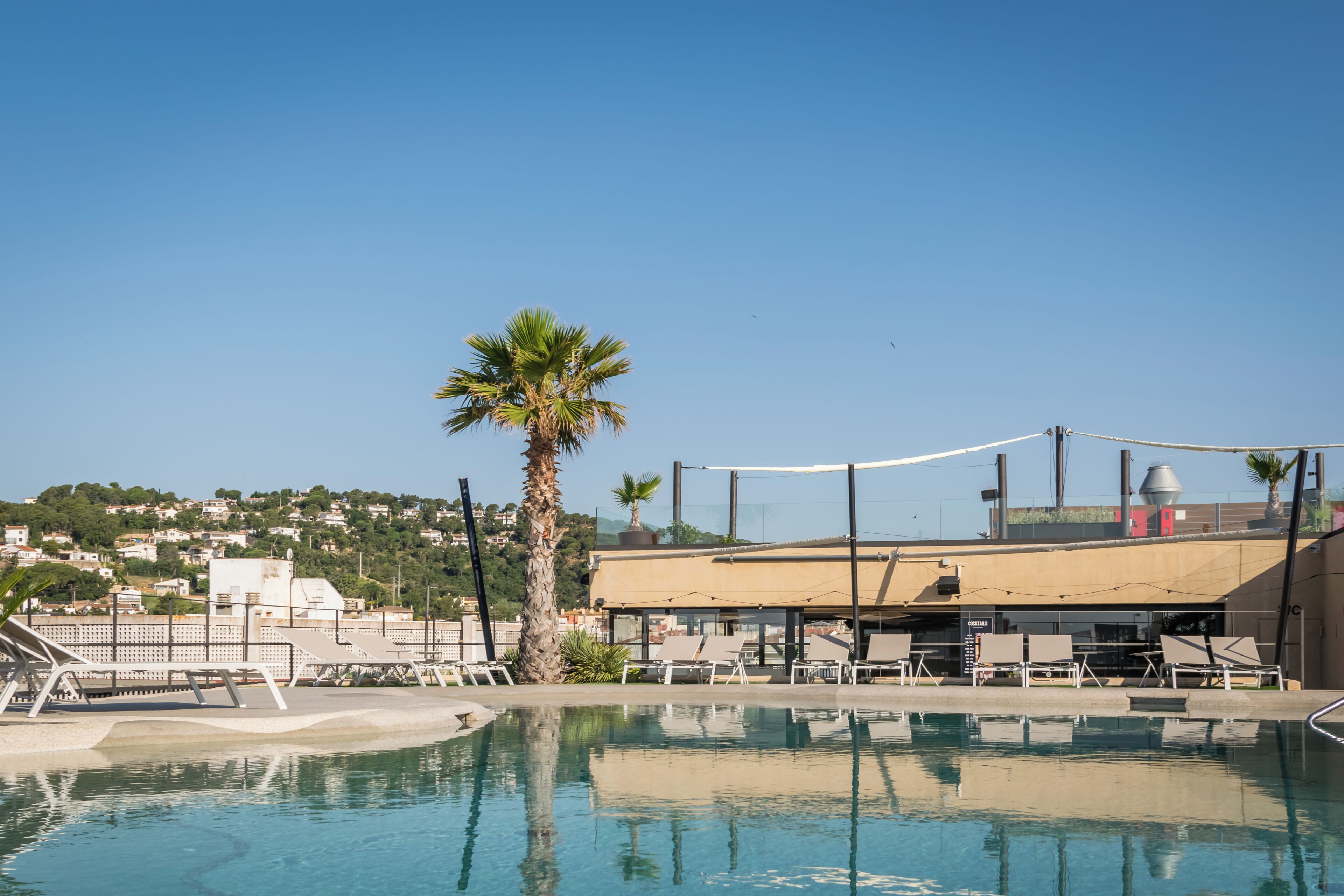Ein Swimmingpool mit Liegestühlen, einer Palme und einem Gebäude mit Dach im Hintergrund.