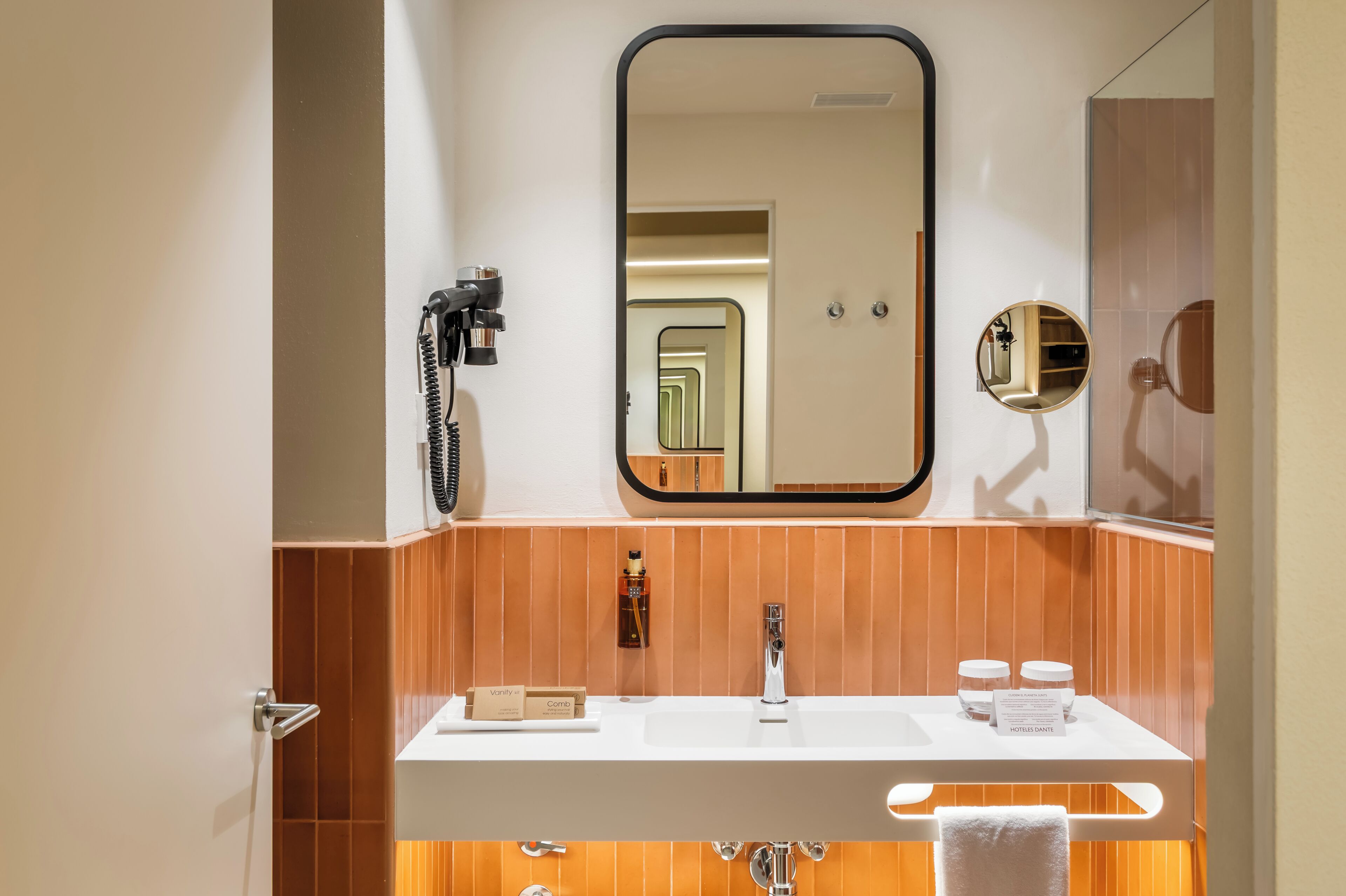 Un baño con un lavabo blanco, un espejo, un secador de pelo y un tendedero para toallas.