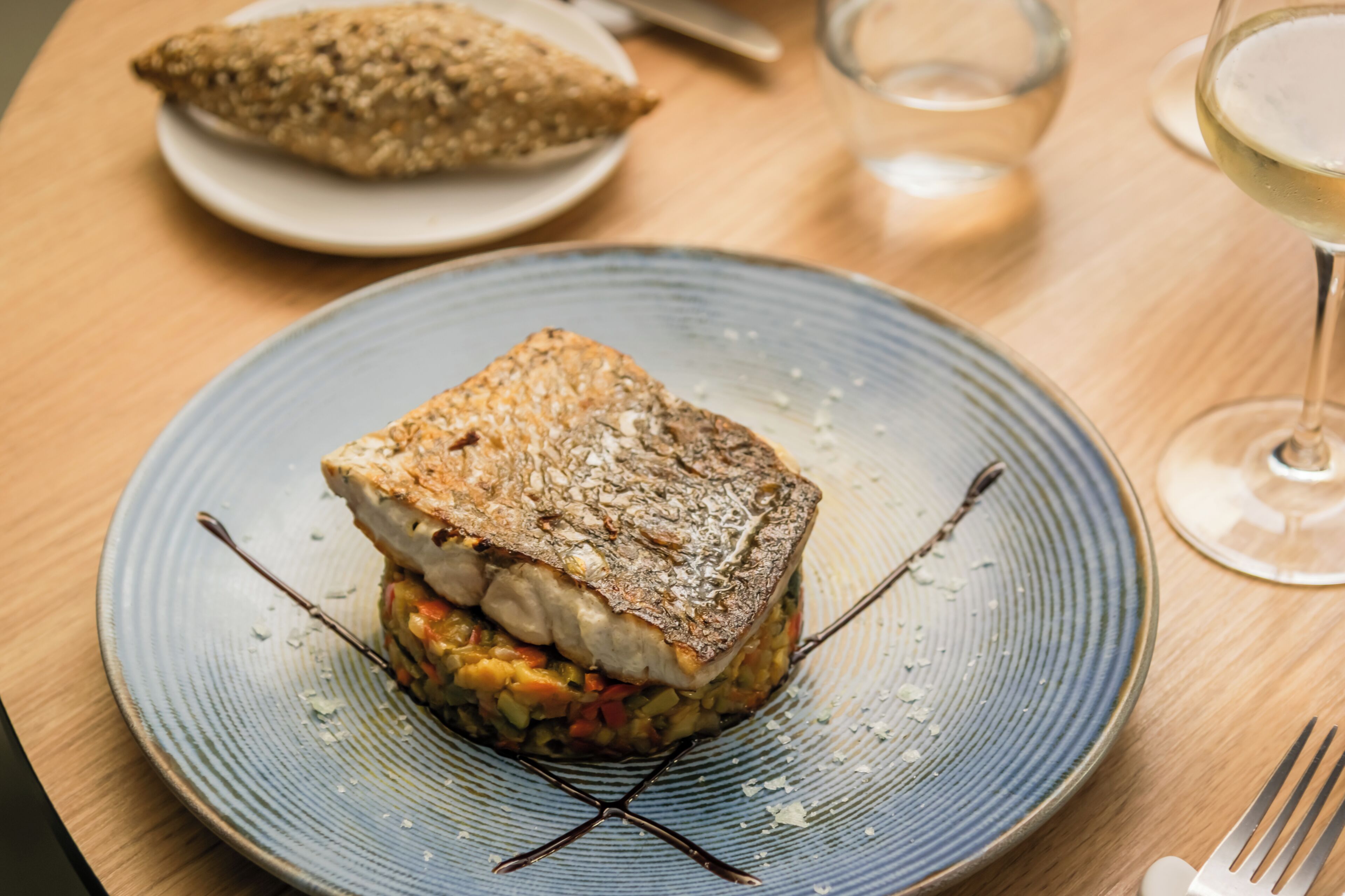 A plate with a grilled fish sandwich and a slice of bread on a table.