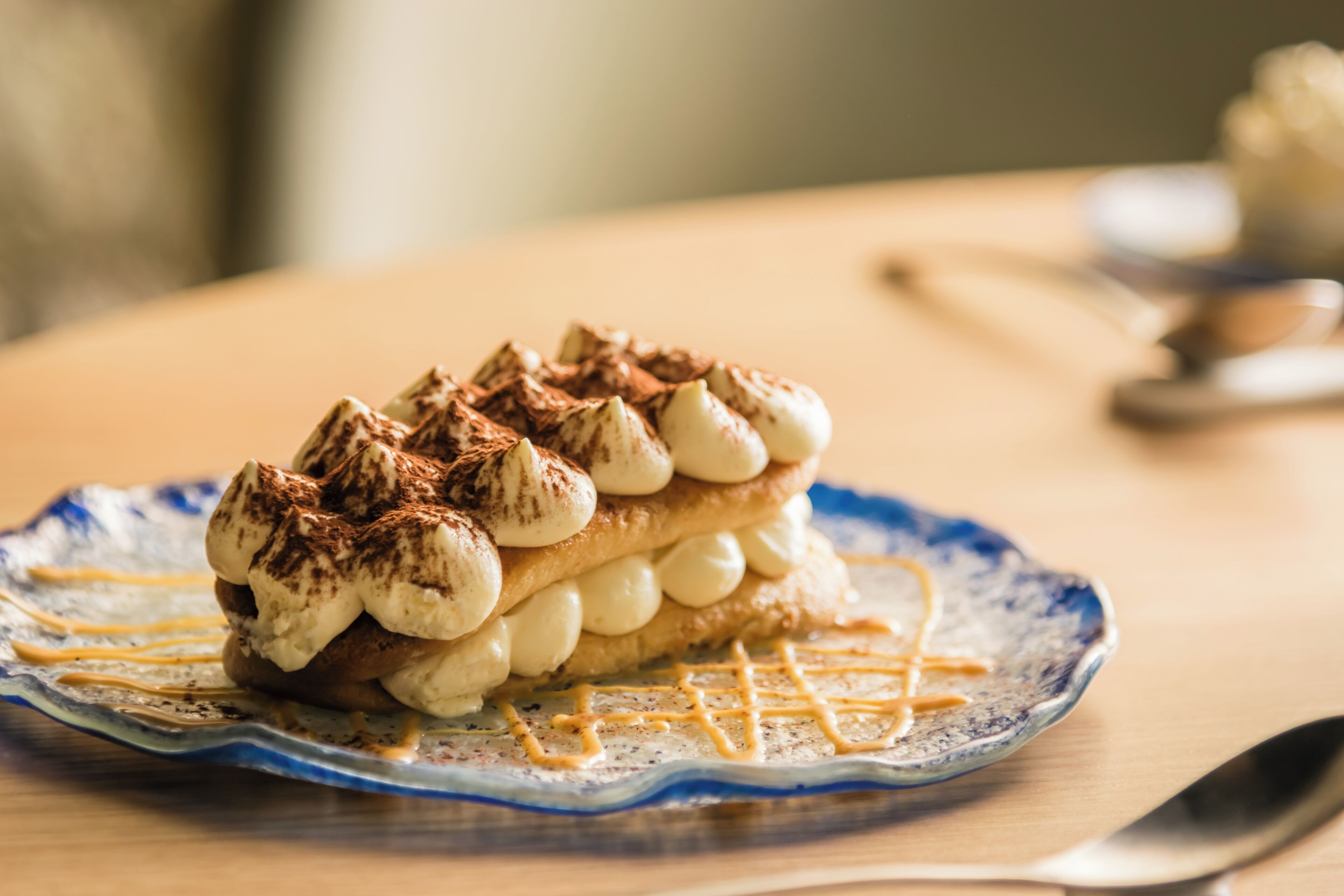 Een dessert op een bord, met een lepel en een kom op de achtergrond.