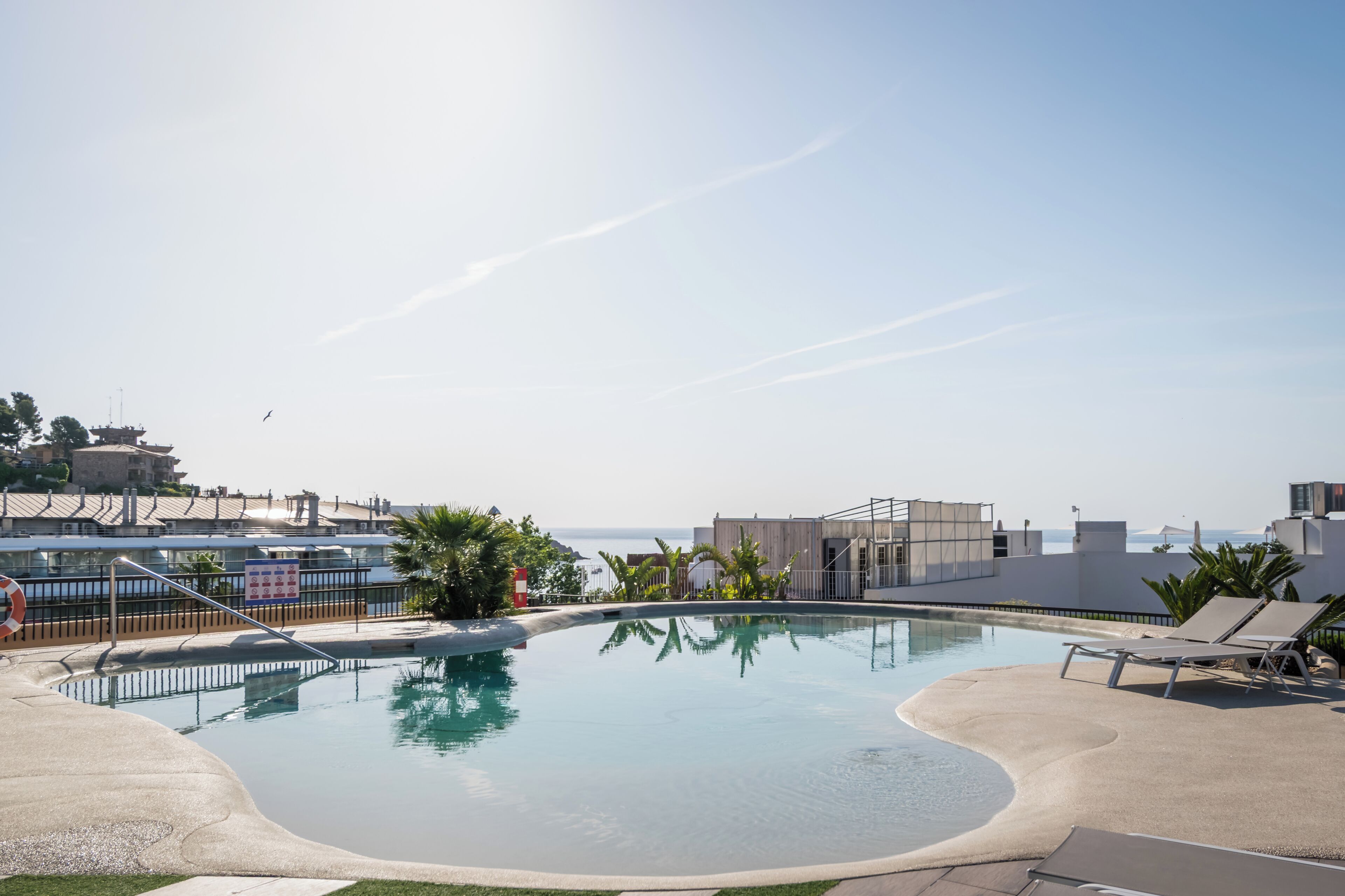 A pool area with a clear view of the sea, lounge chairs, and a lifebuoy.