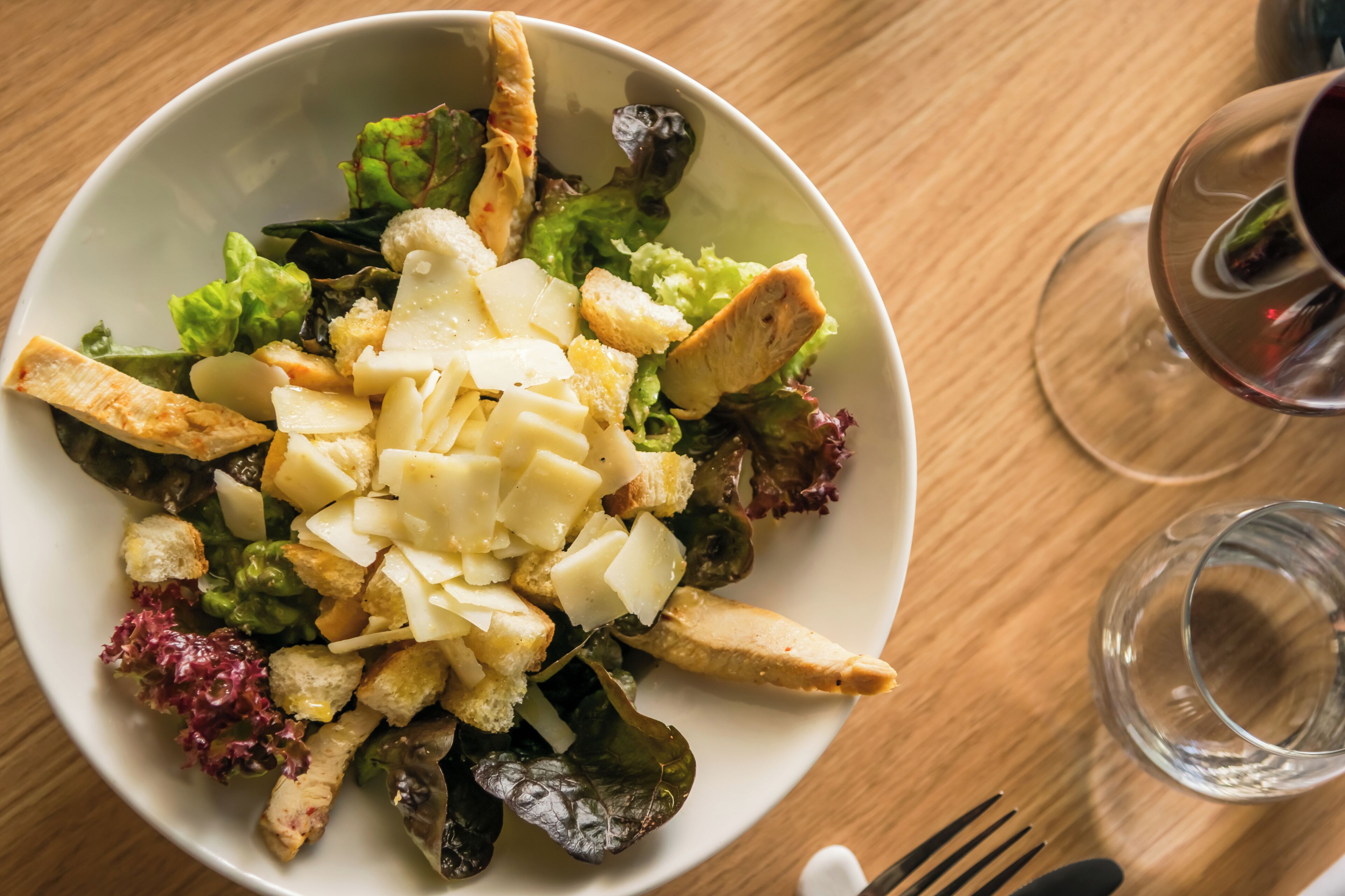 Un saladier rempli de salade, avec des croûtons et du fromage, posé sur une table en bois.