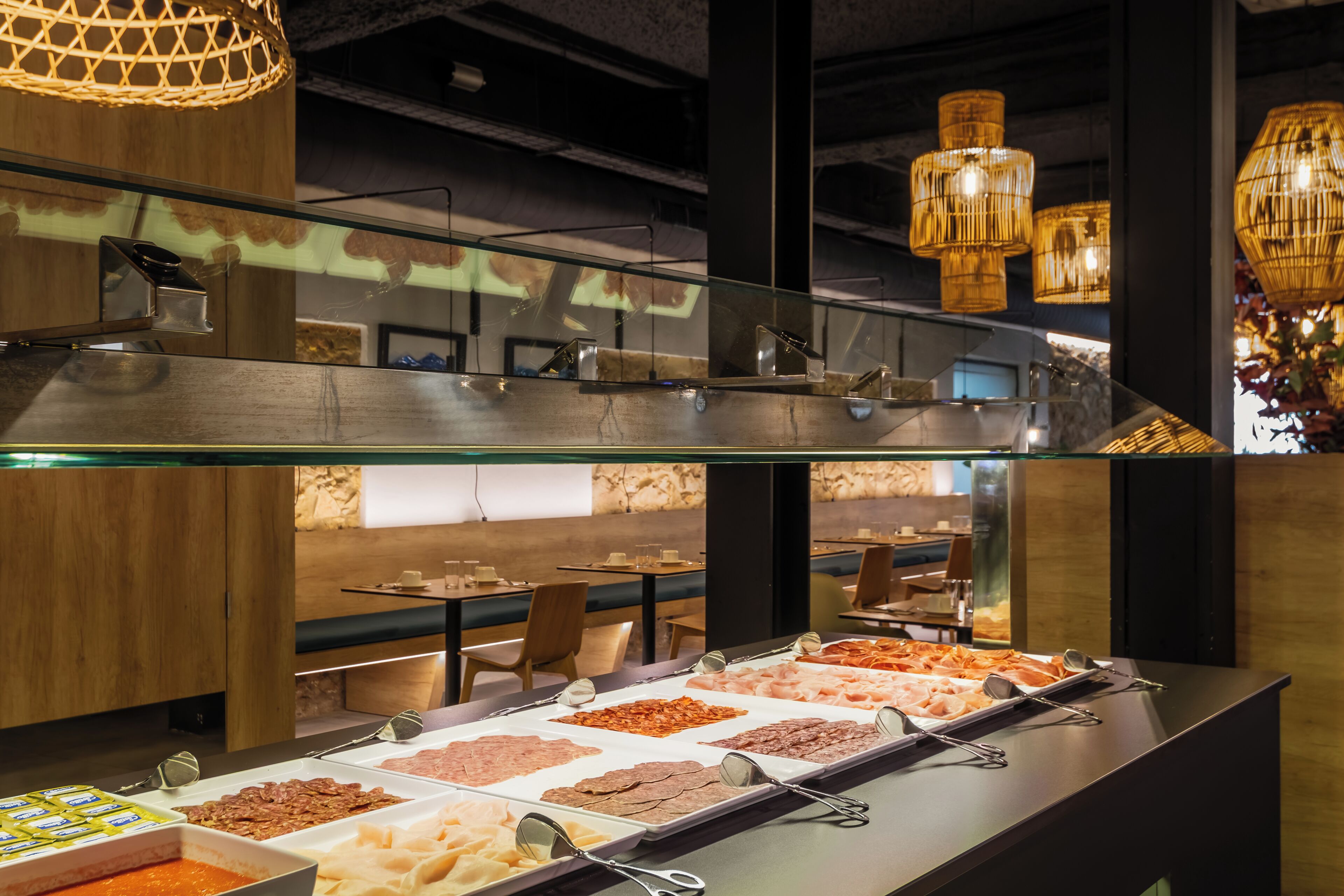 Zona de bufé con varias estaciones de comida y barandilla de cristal con vistas al comedor.