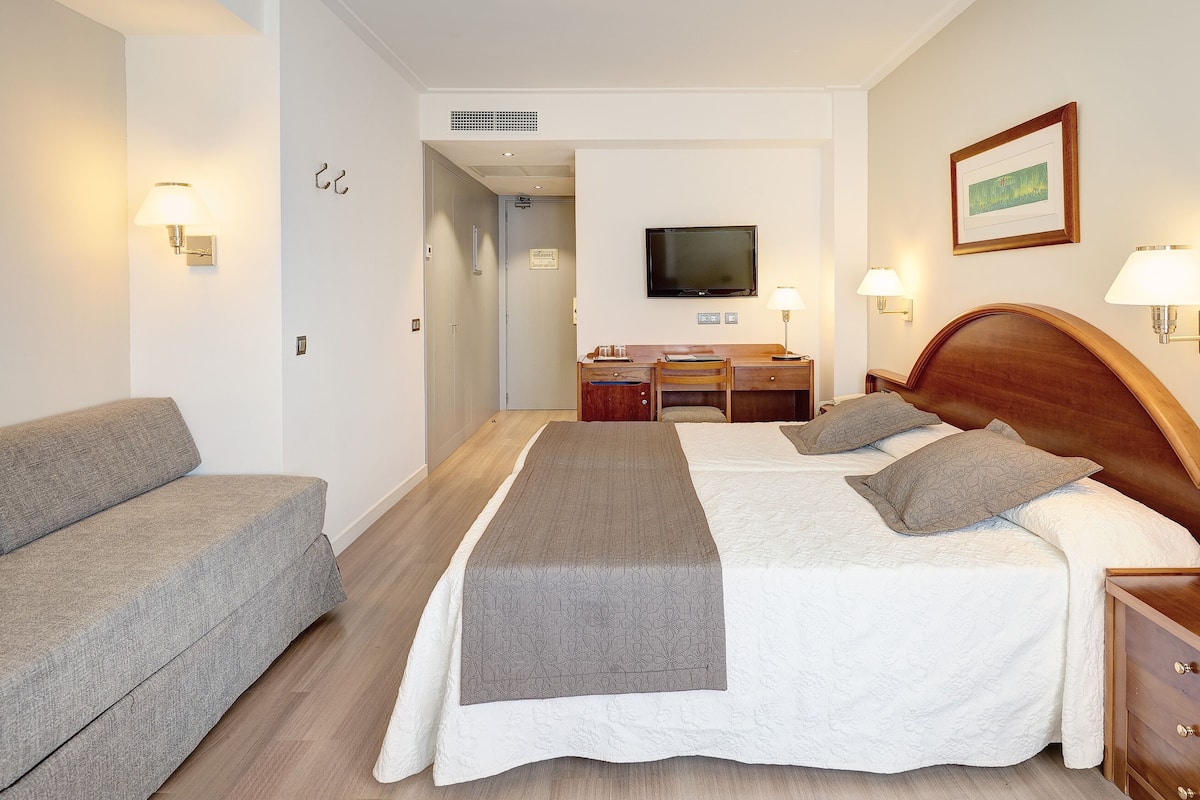 Ein Hotelzimmer mit zwei Betten, einem Schreibtisch, einem Fernseher und einem Sofa.
