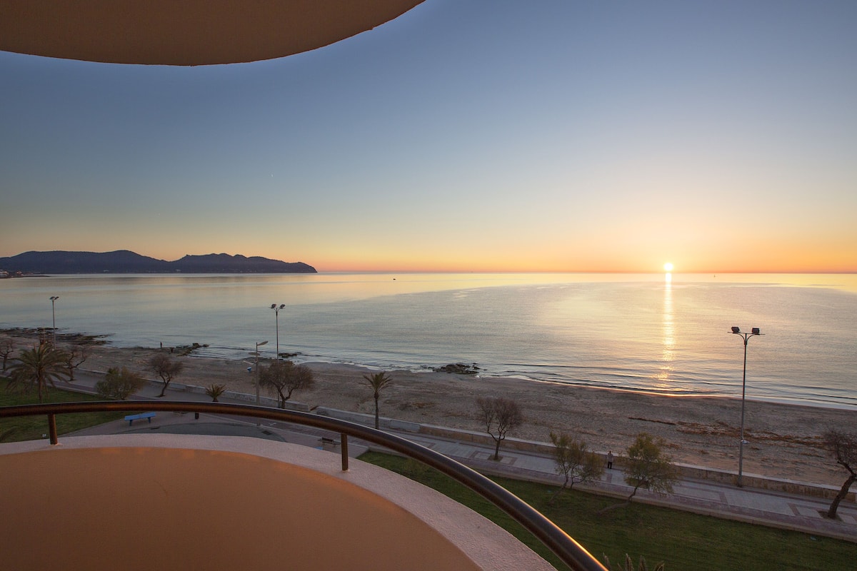 Sonnenuntergangblick von einem Balkon mit Blick auf einen Strand, bewölkter Himmel.
