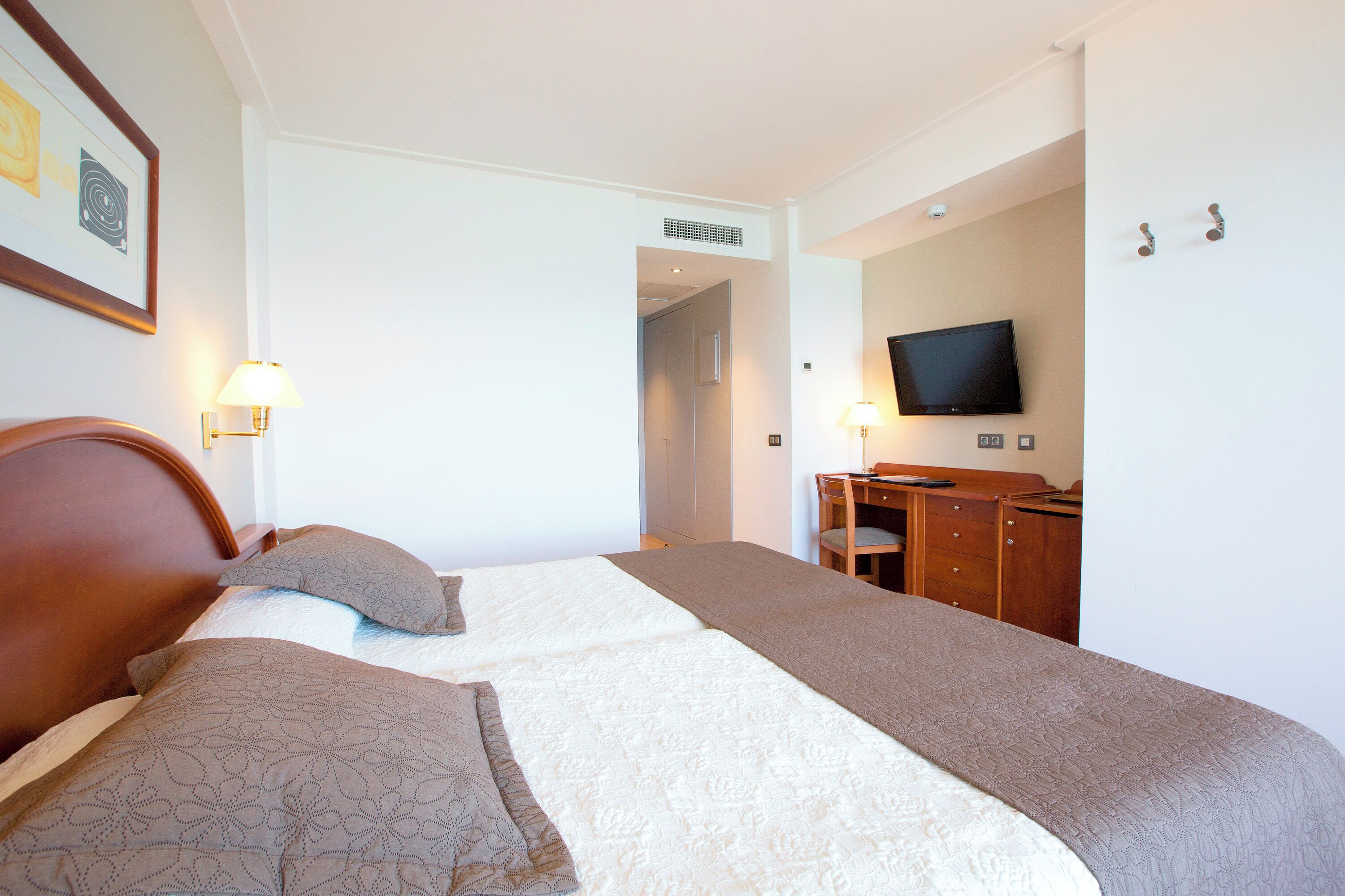 A hotel room with two beds, a desk, a television, and a door leading to another room.