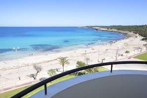 Une vue sur la plage depuis un balcon doté d’une balustrade, avec une eau d’un bleu limpide et une plage de sable.
