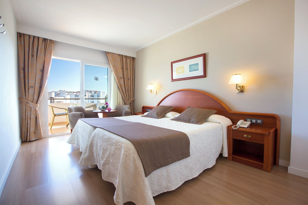 Ein Hotelzimmer mit einem großen Bett, Nachttischen, einem Sessel, einem Schreibtisch und Blick auf die Stadt.
