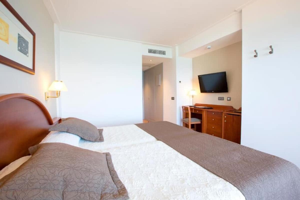 Ein Hotelzimmer mit zwei Betten, einem Fernseher, einem Schreibtisch und einem Sessel.
