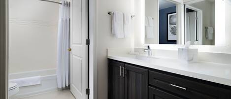 A modern bathroom with a walk-in shower, a large mirror, dark wooden cabinets, and a white countertop.