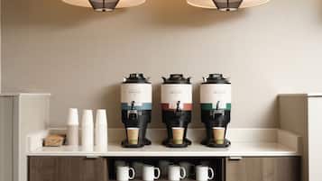 Eine Kaffeestation mit vier Kaffeemaschinen, Stapeln Einwegbechern und einer Reihe Tassen auf einer Theke.