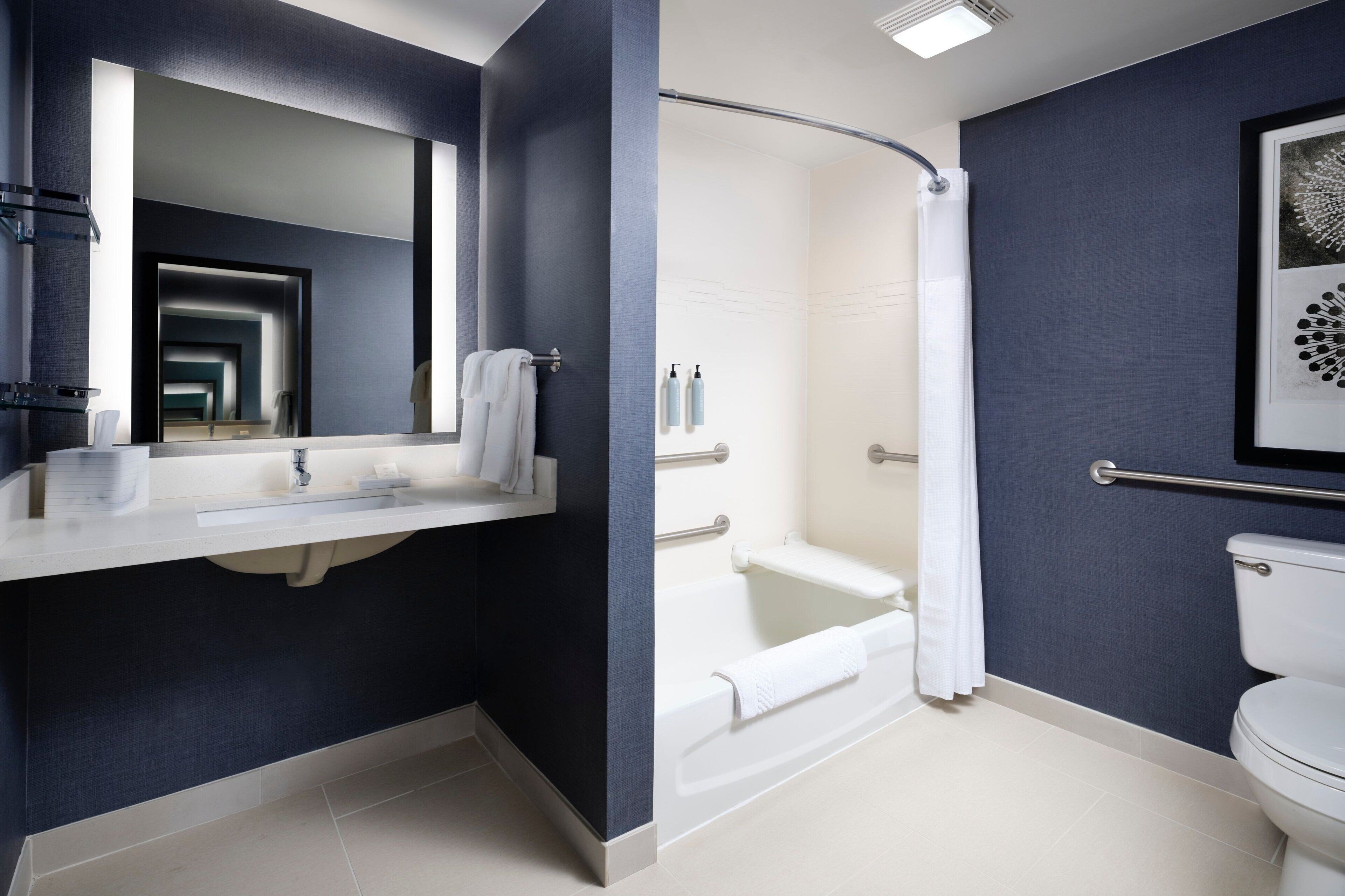 A modern bathroom with a white sink, mirror, and toilet, a shower with a glass door, and a dark blue accent wall.