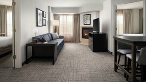 Een moderne hotelkamer met een bank, een eettafel met stoelen, een flatscreen televisie, een open haard en kunstwerken in lijsten aan de wanden.