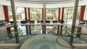Una amplia piscina cubierta con un jacuzzi central, rodeada de zonas de estar y grandes ventanales que ofrecen vistas al exterior.