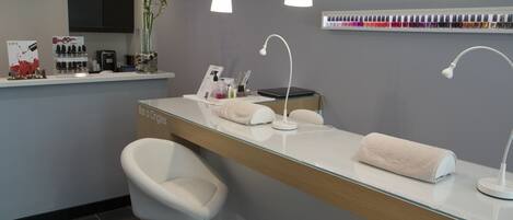 A modern reception area with a glass counter, white chairs, a reception desk, a wall-mounted color palette, and pendant lighting.