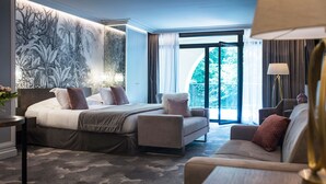 Habitación de hotel con cama, sofá, escritorio y un ventanal con vistas a zonas verdes.
