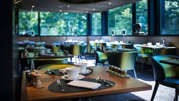 A modern dining area with tables set for two, featuring black placemats, white cups, and a variety of tableware.