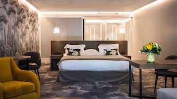 Een moderne hotelkamer met een groot bed, een bureau, een gele fauteuil en een bloemenvaas.