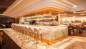 Un área de bar moderna con encimera de mármol, taburetes y una gran variedad de botellas y copas.