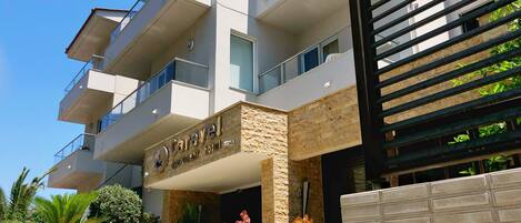 A modern hotel with a sign reading "Caravel Apartment Hotel". It features a stone facade, multiple balconies, and decorative vases with flowers.