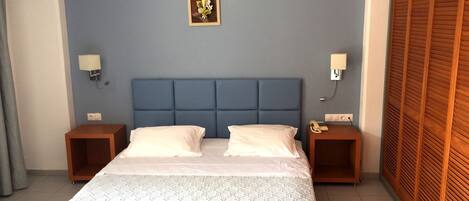 A bedroom with a blue headboard, two bedside tables with lamps, a bed with a patterned bedspread, and a wooden wardrobe.