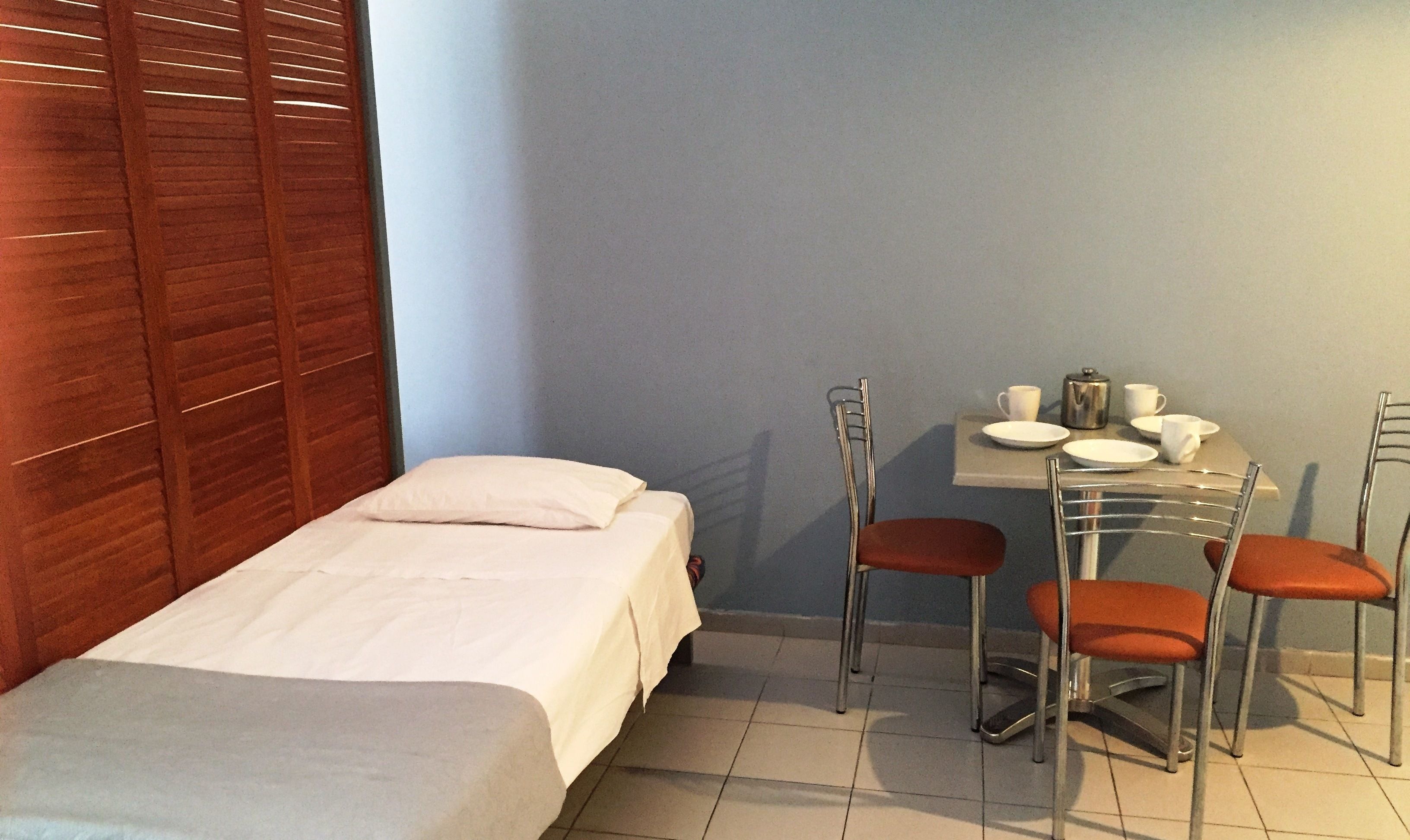 A small hotel room with a single bed, a table with chairs, and a kettle.