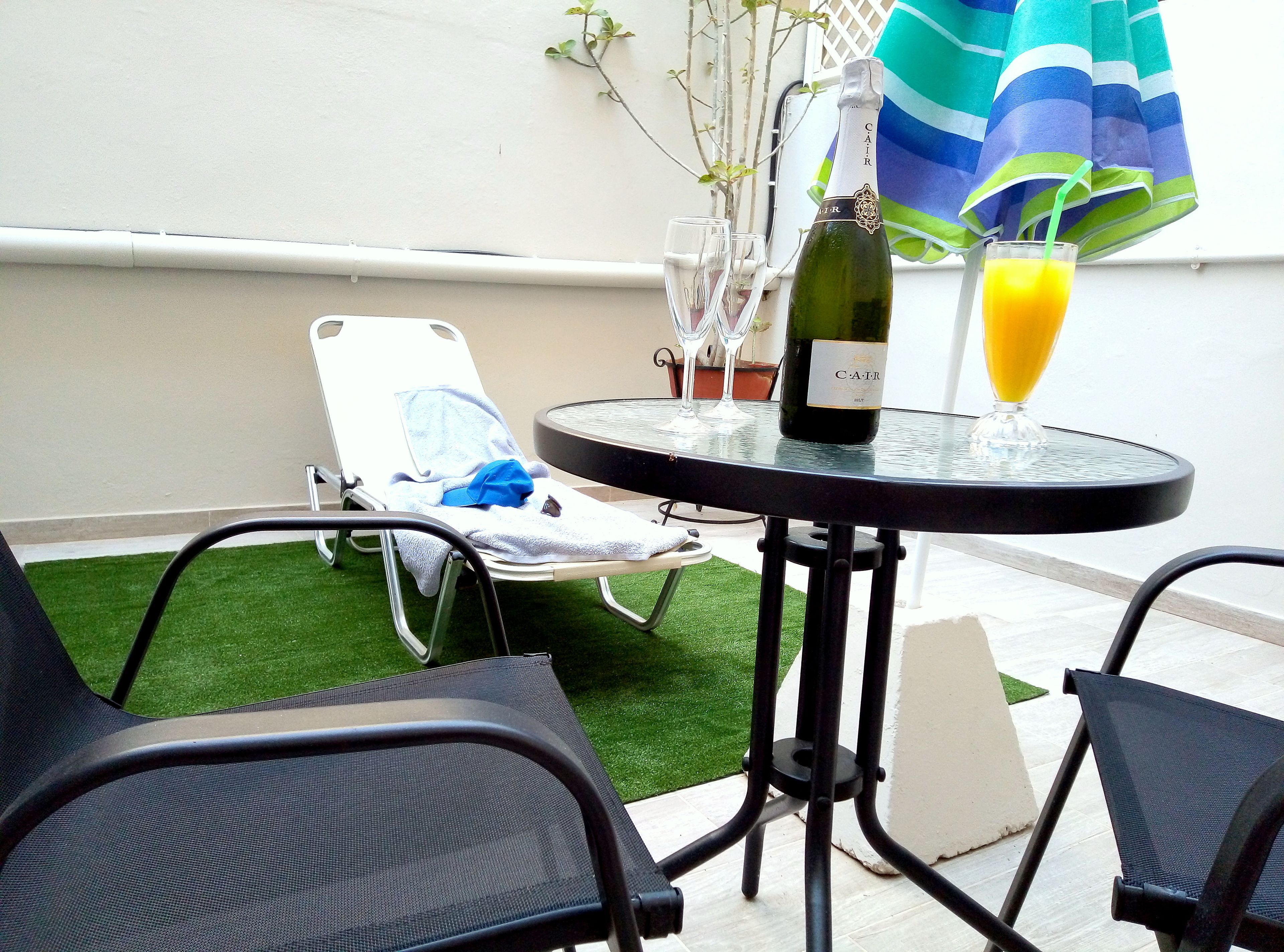A small outdoor seating area with a table, chairs, and a bottle of wine.