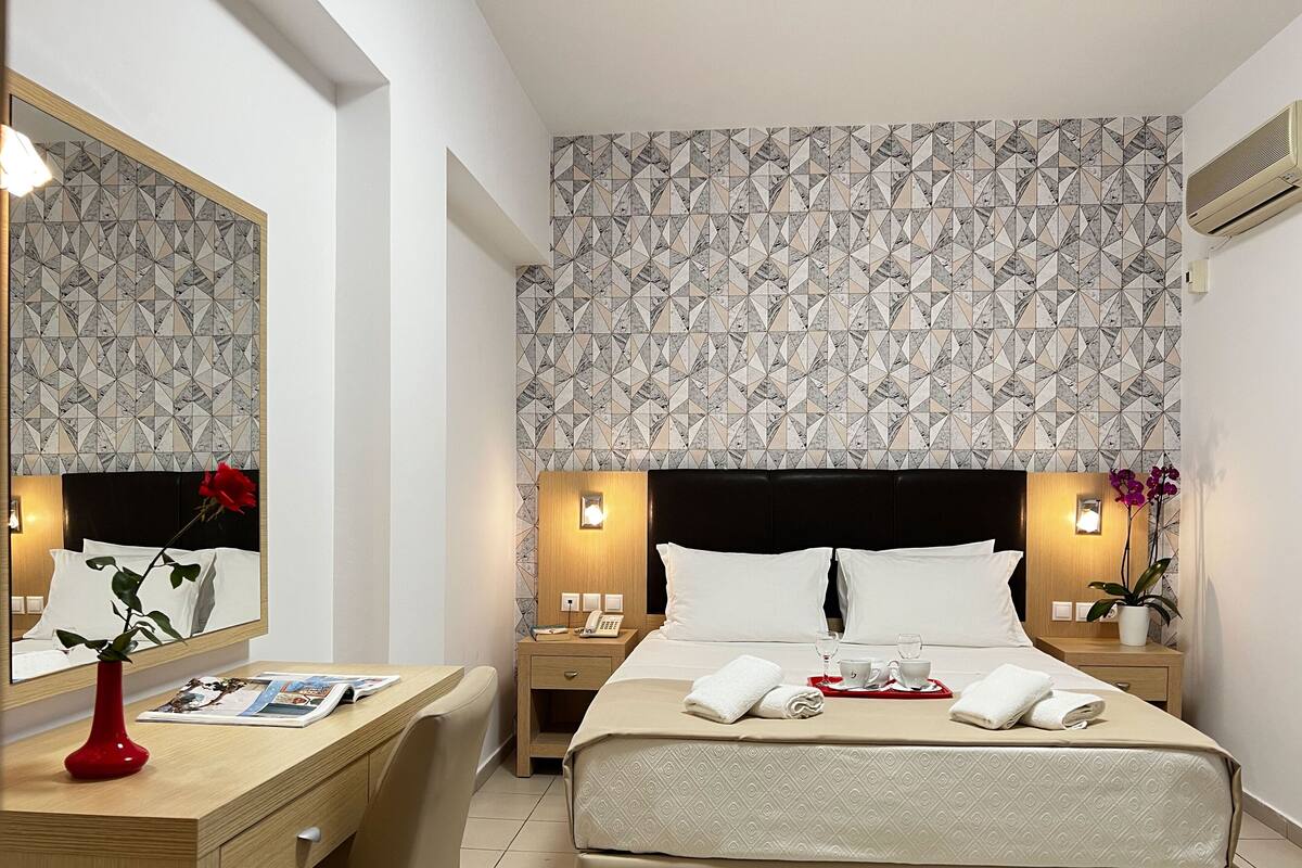 Een hotelkamer met een bed, nachtkastjes, een bureau, een spiegel en een behang met patroon.