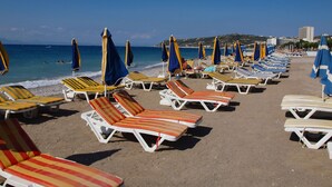 Une plage bordée de rangées de transats et de parasols, un ciel dégagé et une mer calme.