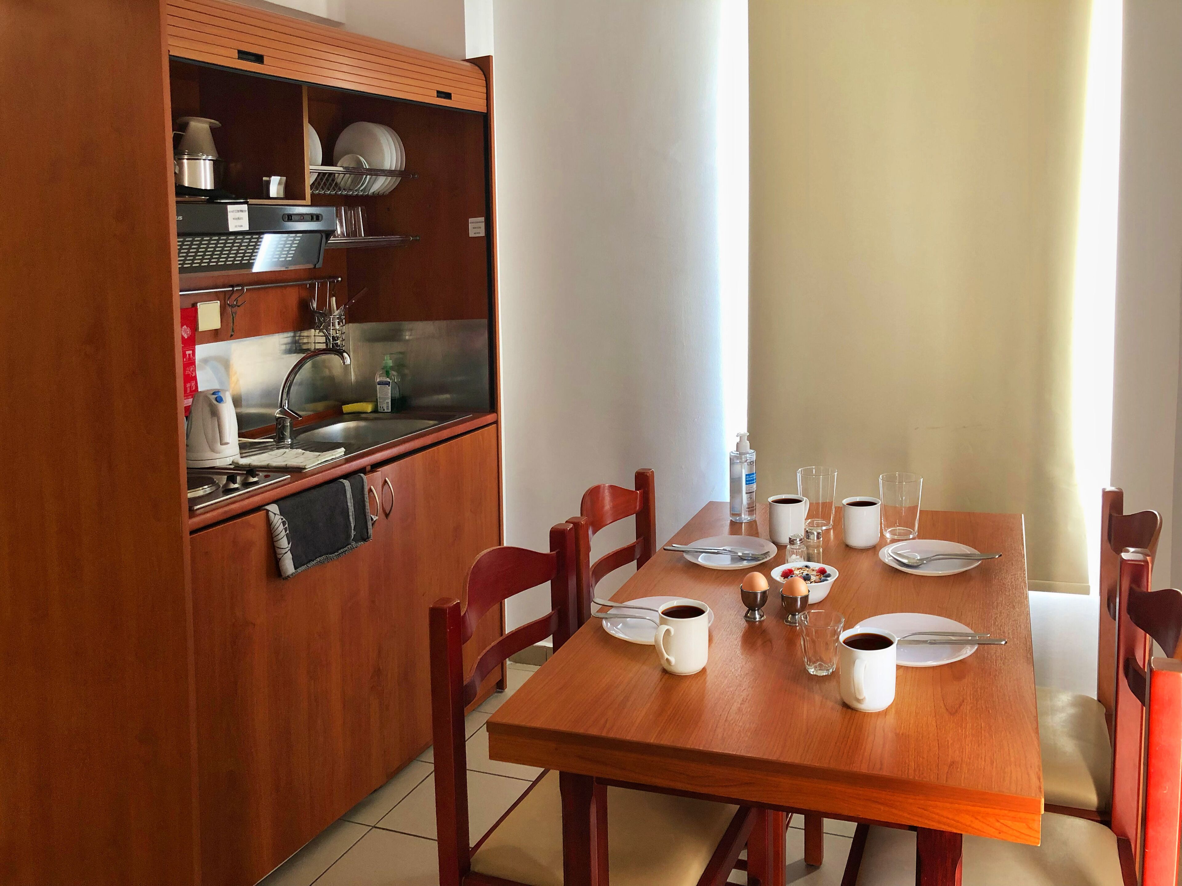 A compact kitchen with a dining table set for two, including plates, cups, and cutlery.