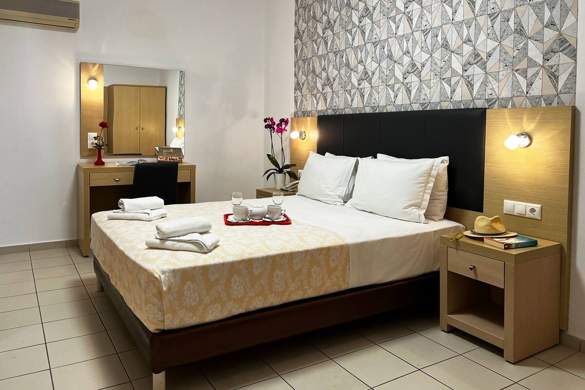Een hotelkamer met een bed, nachtkastje, bureau, stoel, spiegel en een kamer met een patroon op de muur.