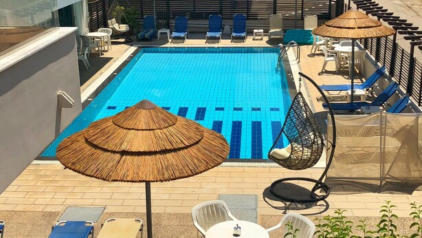 Un espace piscine sur le toit, avec des carreaux bleus, des chaises longues et des parasols en chaume.