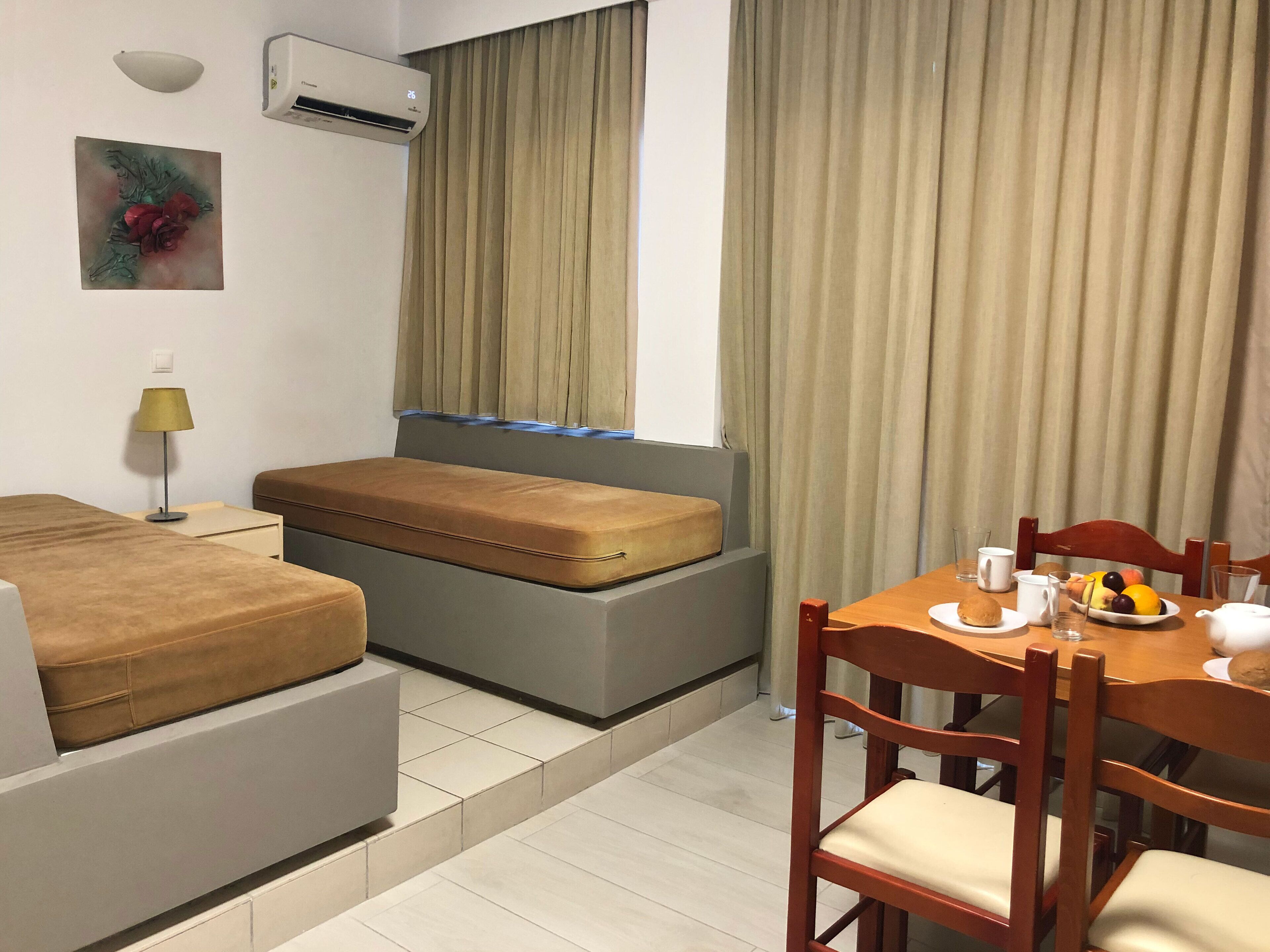 Ein Hotelzimmer mit Bett, Schlafsofa, Esstisch mit Stühlen, Obstschale und Wandklimaanlage.