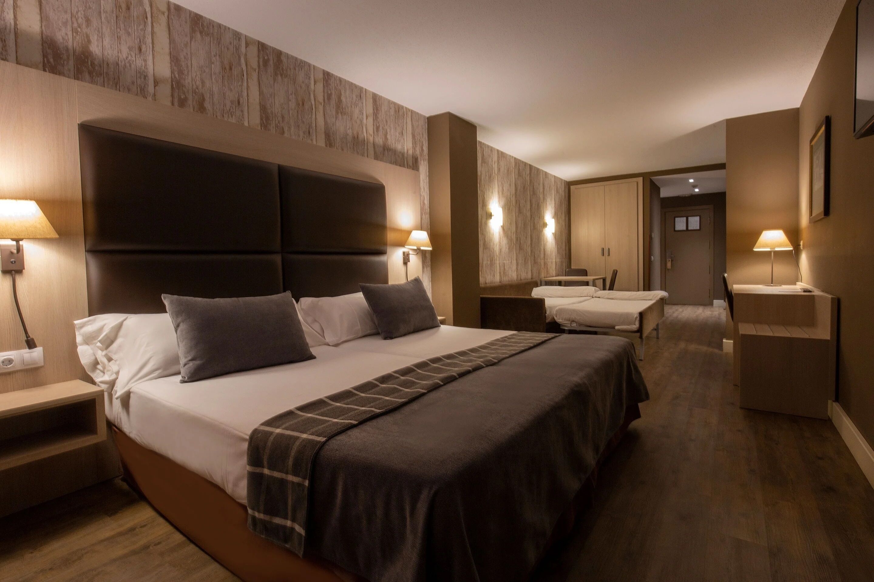 A hotel room with a large bed, bedside tables, a desk, and a wardrobe.