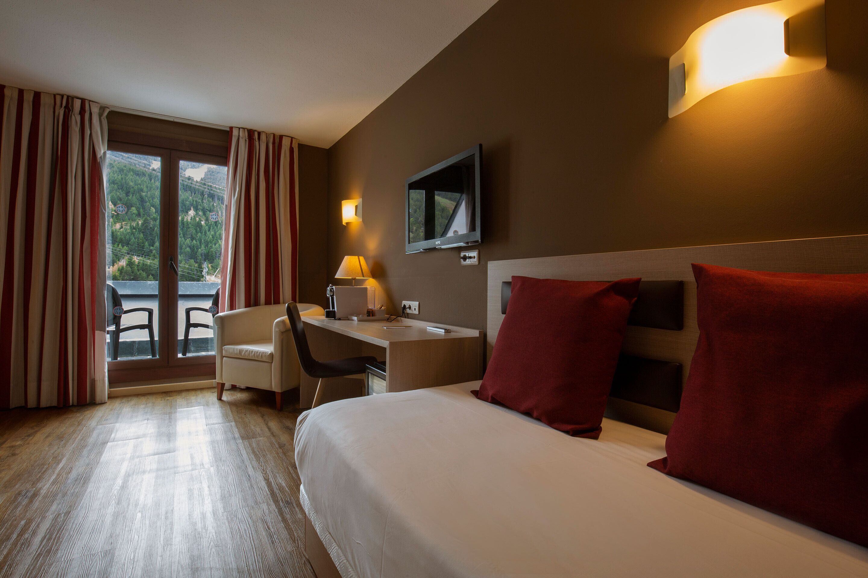 A hotel room with a bed, desk, chair, and a TV on the wall.