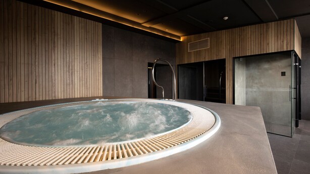 A modern spa area with a hot tub, wooden panel walls, and a sleek, metallic shower enclosure.