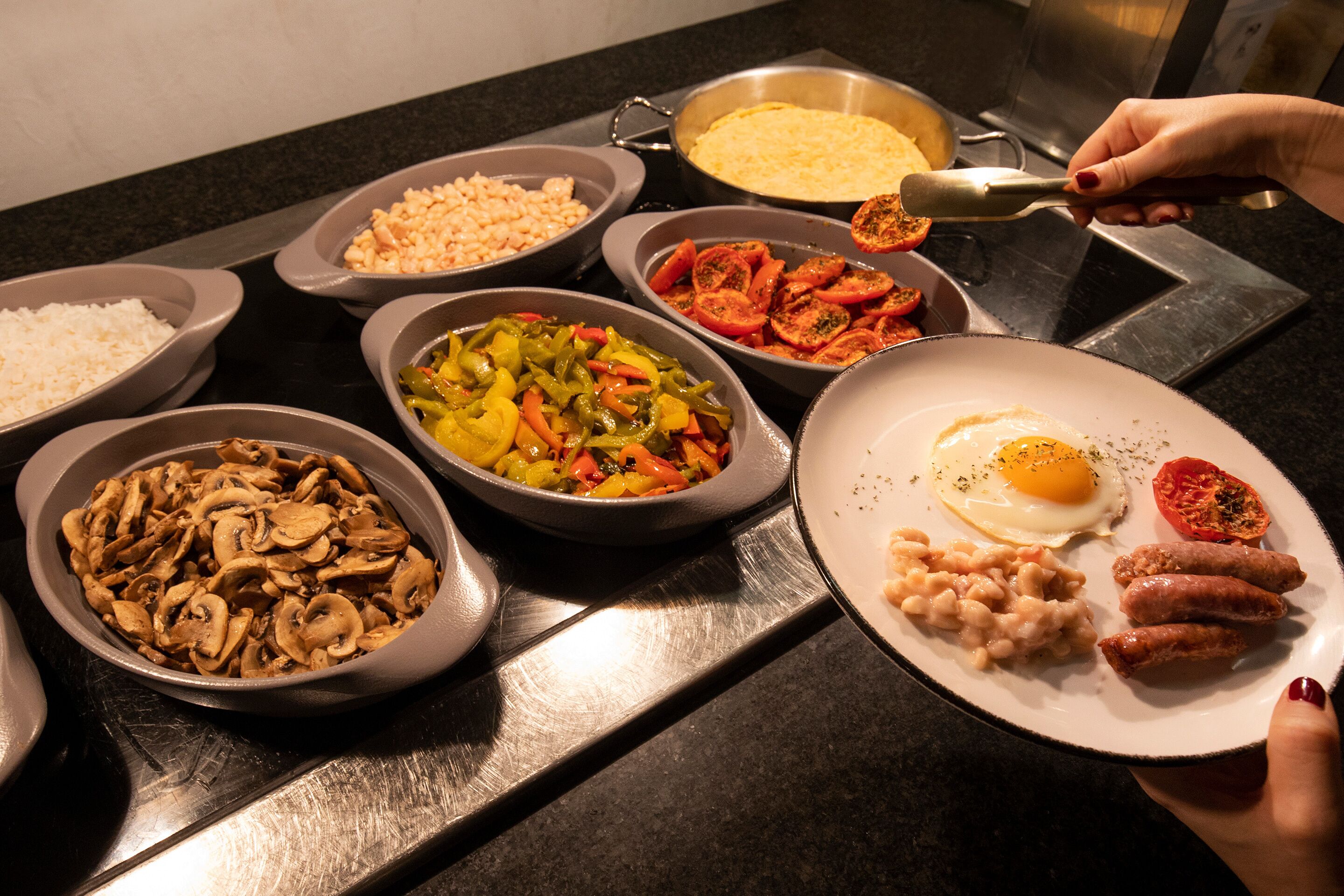 A variety of food items on a table, including rice, beans, mushrooms, bell peppers, tomatoes, and a plate with eggs, sausages, and beans.