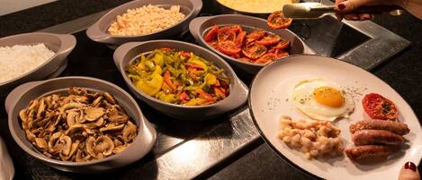 A variety of food items on a table, including rice, beans, mushrooms, bell peppers, tomatoes, and a plate with eggs, sausages, and beans.