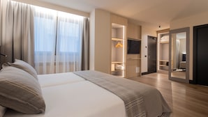A modern hotel room with a large bed, a walk-in closet, a television, and a mirror.