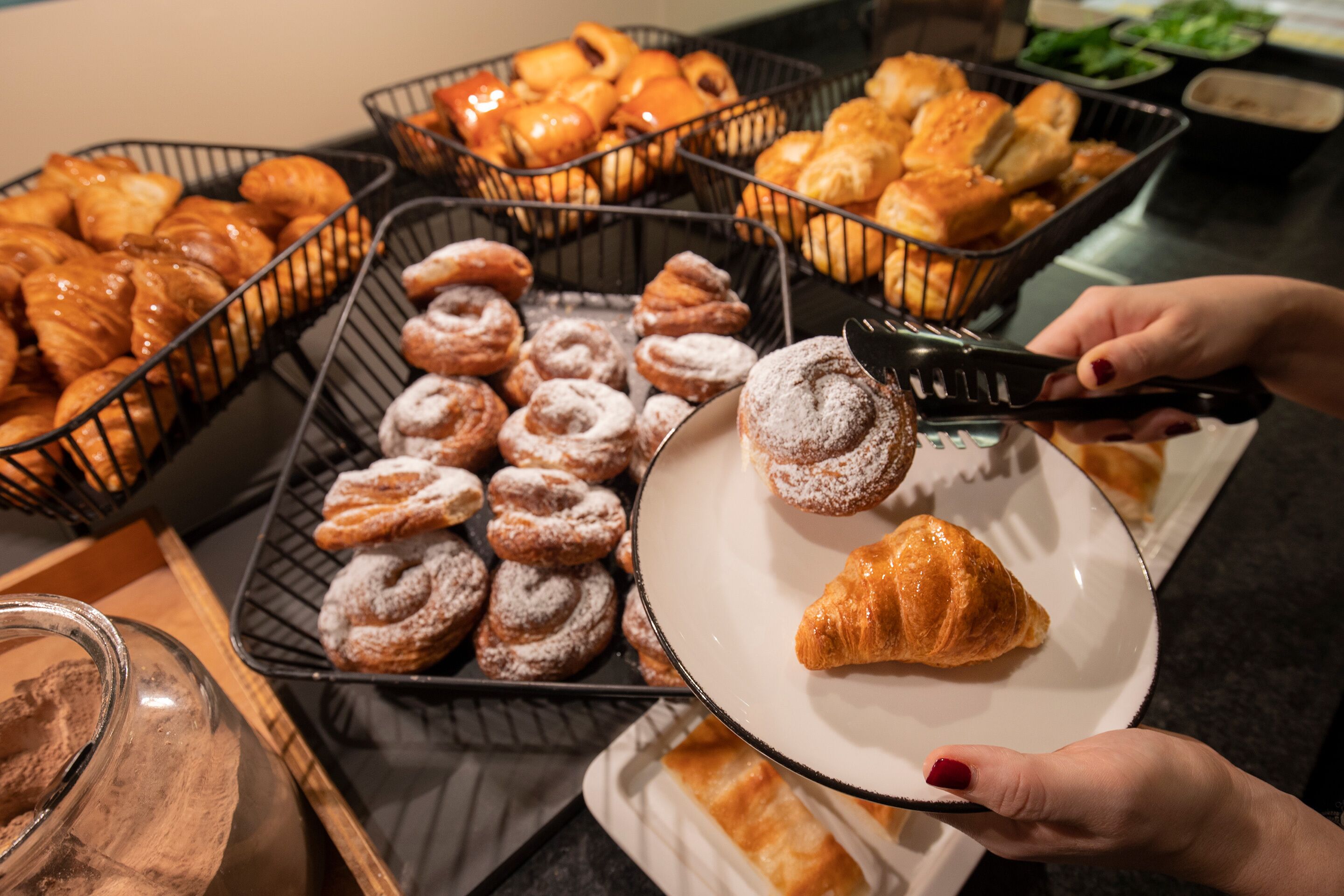 Diverse gebakjes, waaronder croissants, gepresenteerd in mandjes en op een bord, met gebakjes bestrooid met poedersuiker.