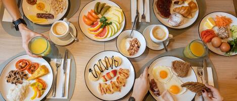 A breakfast buffet with various dishes including eggs, sausages, and fruits.