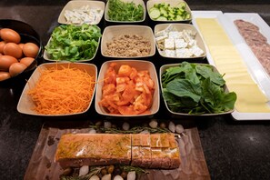 Variedad de alimentos como huevos, zanahoria rallada, tomates, hojas verdes y un trozo grande de carne sobre una tabla de cortar.