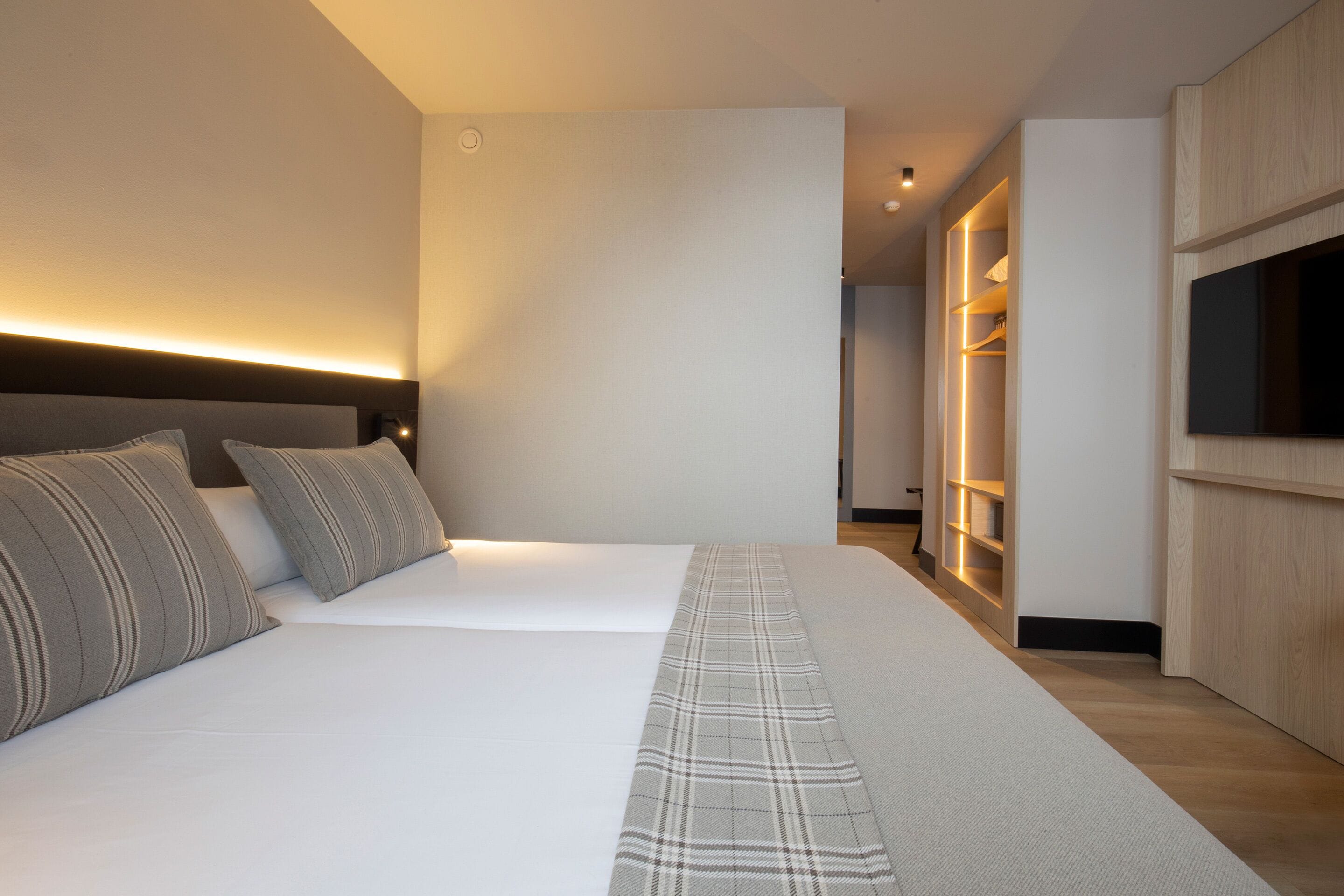 Une chambre à coucher moderne avec un grand lit, une table de chevet, un téléviseur intégré et un dressing.