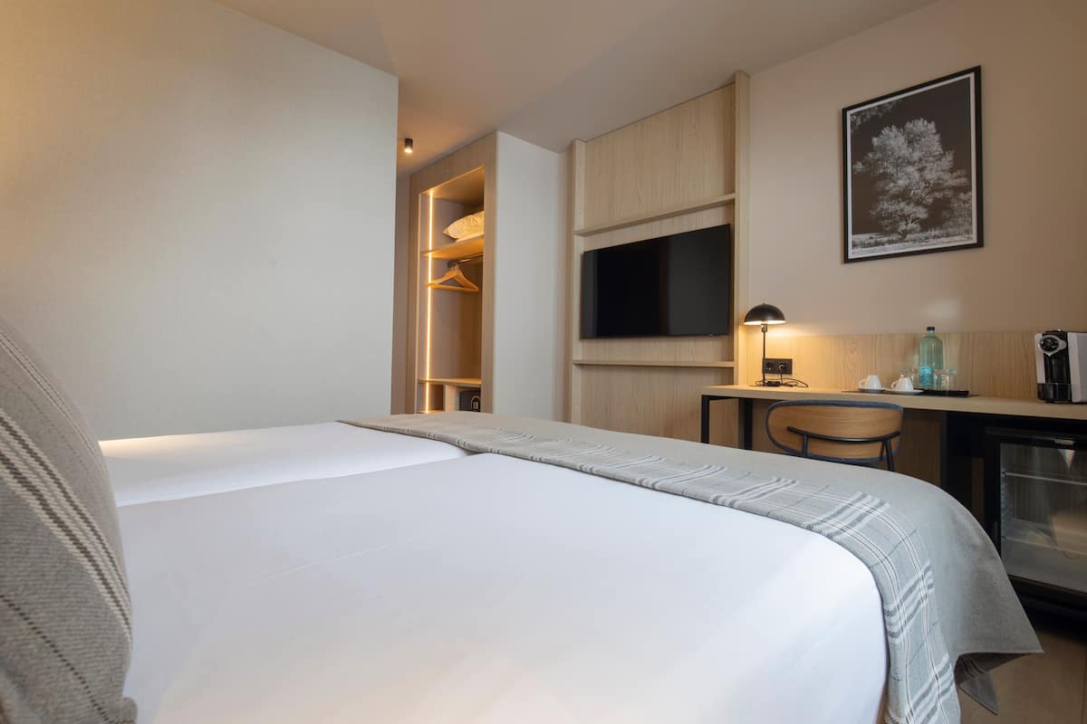 A hotel room with a bed, a desk with a computer, a TV, and a wardrobe.