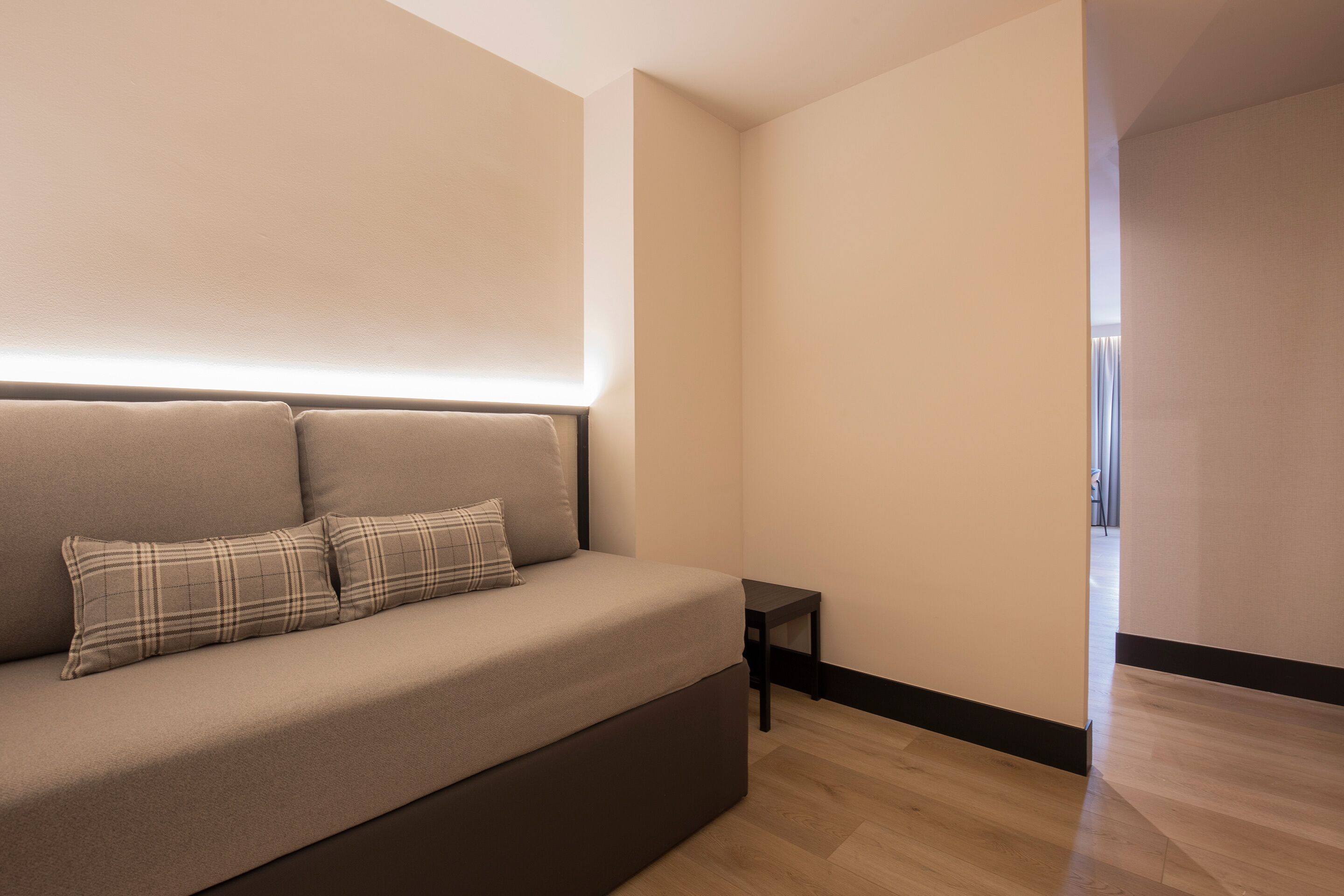 A modern bedroom with a sofa bed, a bedside table, and a large window.