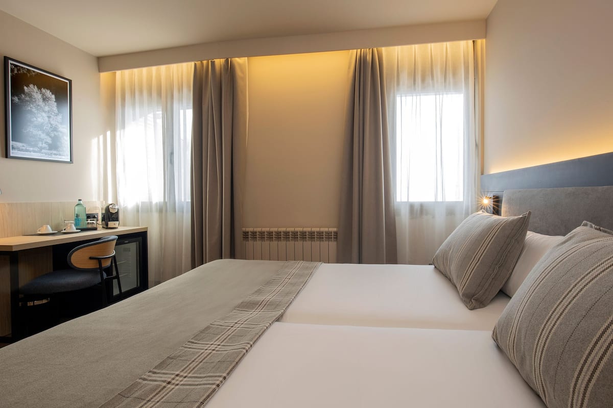 A hotel room with a bed, a desk, a chair, and a radiator.