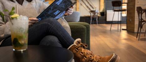 A person sitting on a couch reading a book, with a glass of drink on a table in front.